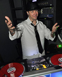 male dj behind console, with hands up and hat on