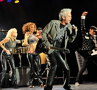 male singer with band belting song with female singers behind him